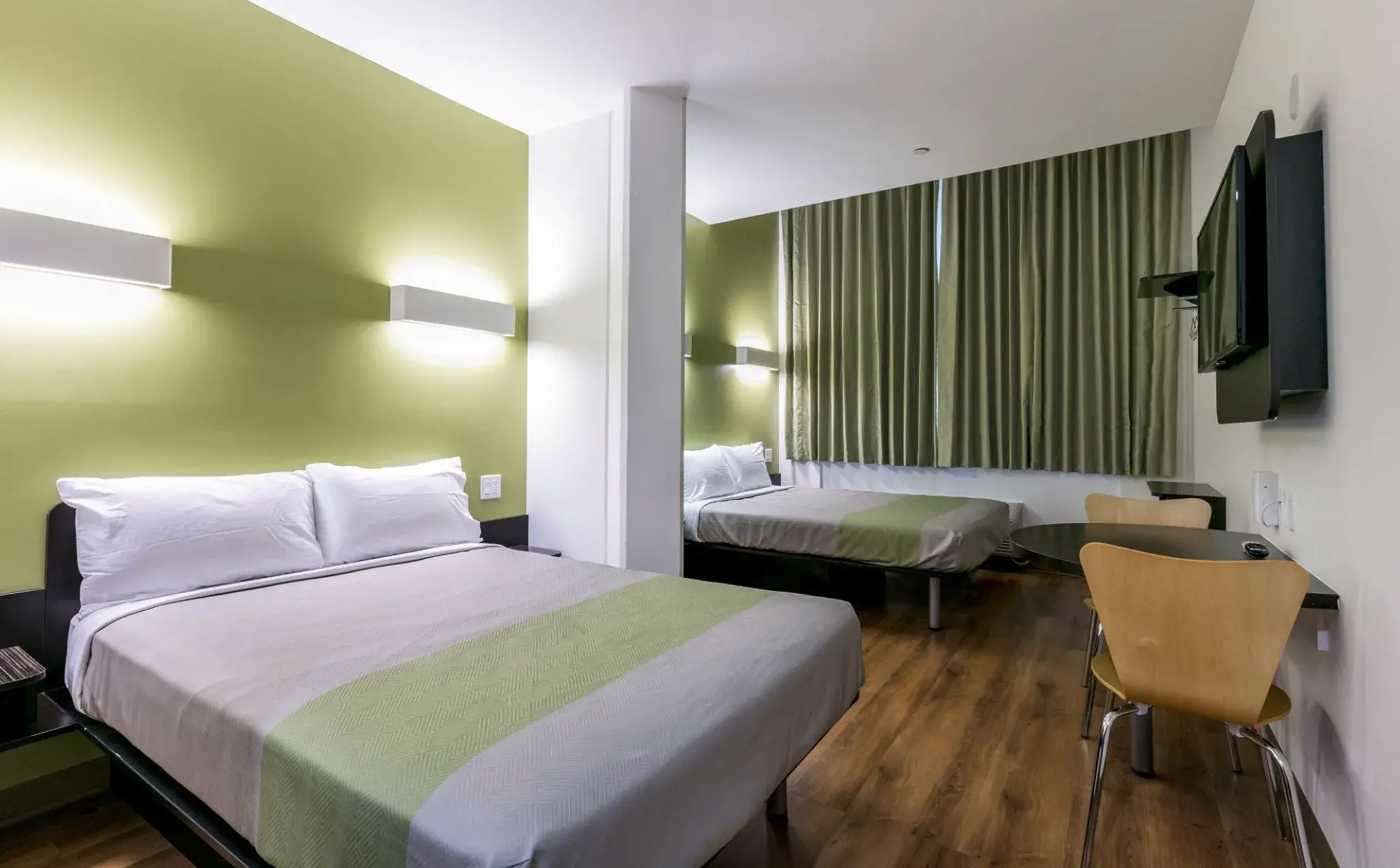 Room with two beds separated by a column, table with chairs and flat-screen TV