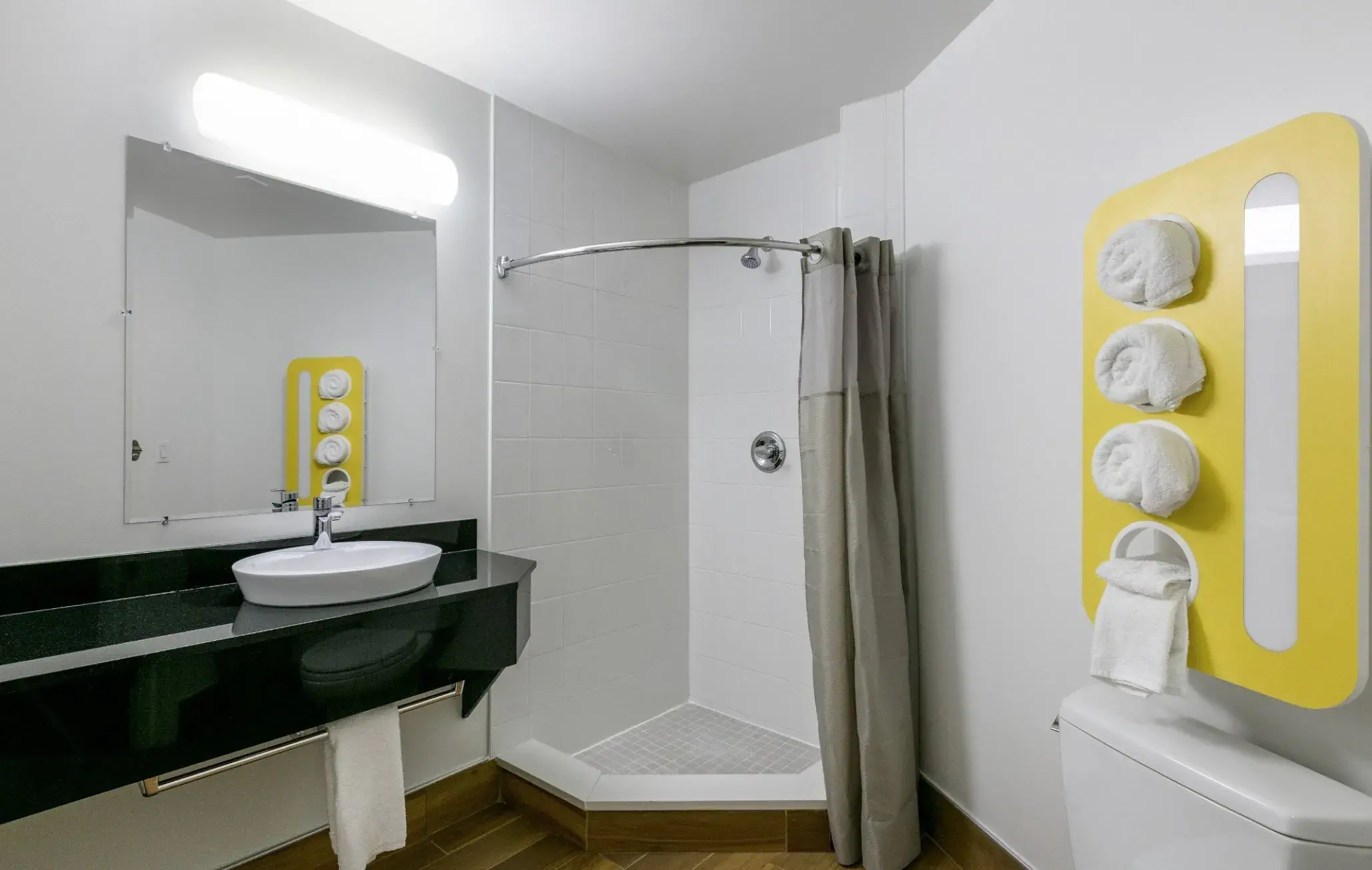 Bathroom with shower, basin on a black countertop and yellow towel rack